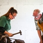 Lady showing gentleman how to blacksmith